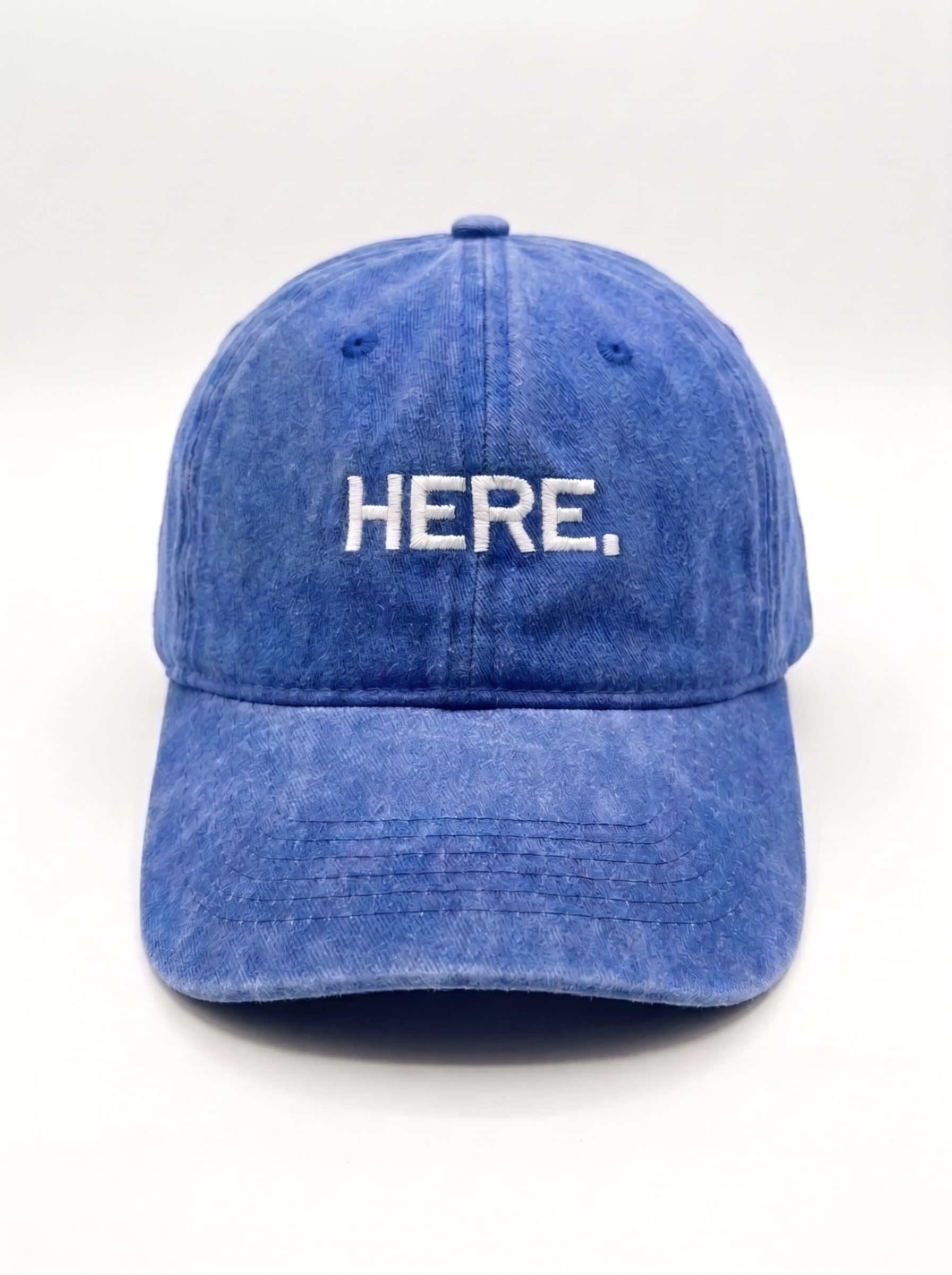 A blue washed cotton baseball cap with the word 'HERE.' embroidered in white capital letters on the front, set against a plain white background.