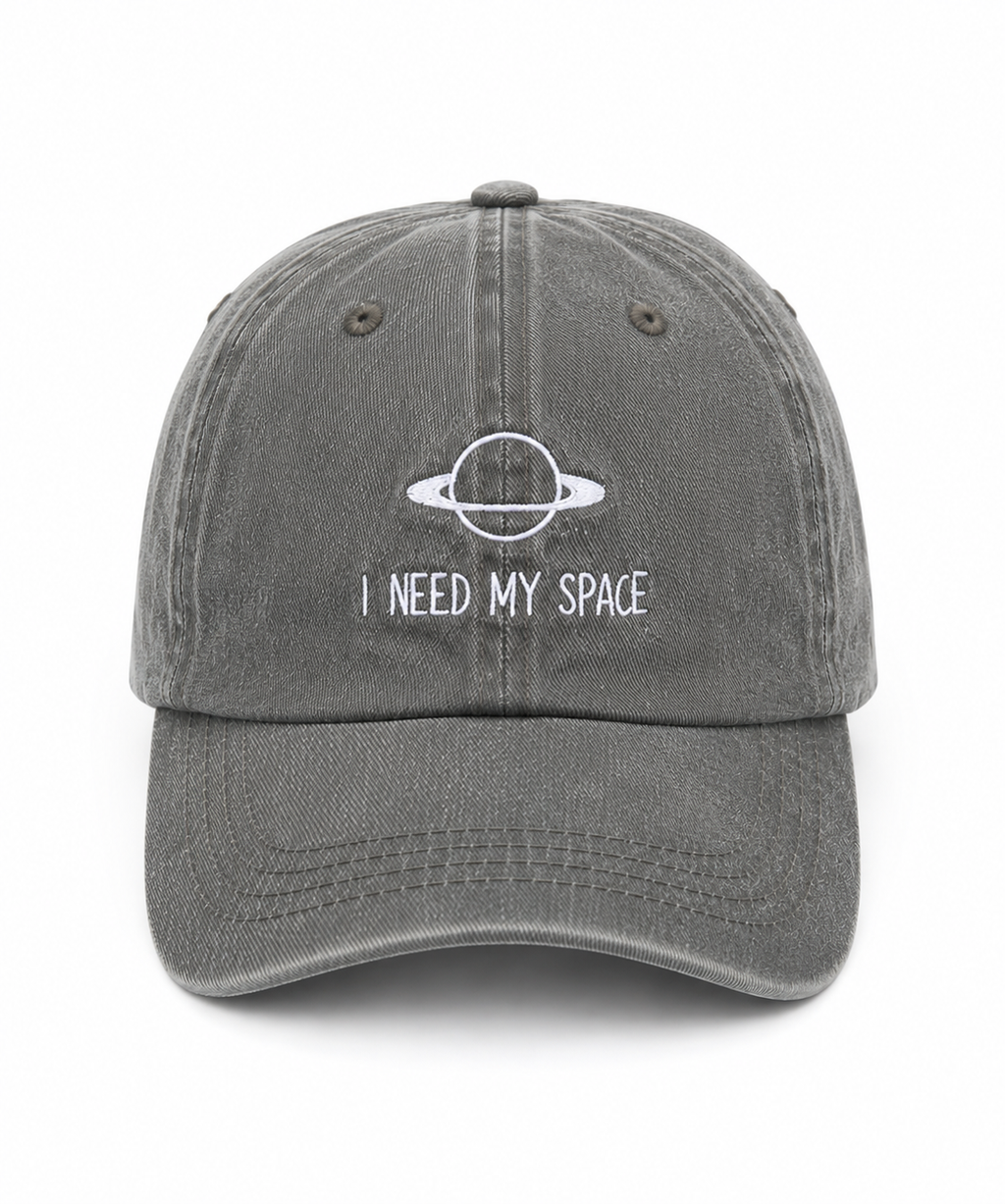 A washed dark gray baseball cap featuring a white embroidered graphic of a ringed planet and the text 'I NEED MY SPACE' on the front, set against a plain white background.