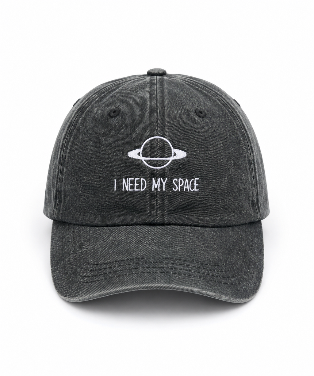A dark gray washed baseball cap with a white embroidered graphic of a ringed planet and the text 'I NEED MY SPACE' on the front, shown against a plain white background.